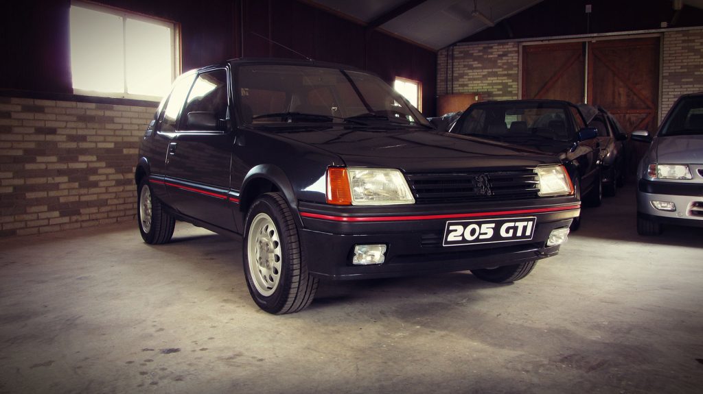 Peugeot 205 GTI 1.6 (115pk), driekwart van voren tegen een donkere gevel