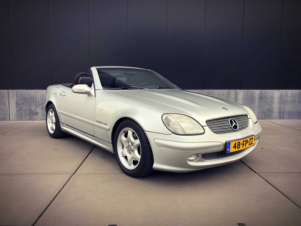 Mercedes-Benz SLK 200K, driekwart van voren tegen een donkere gevel