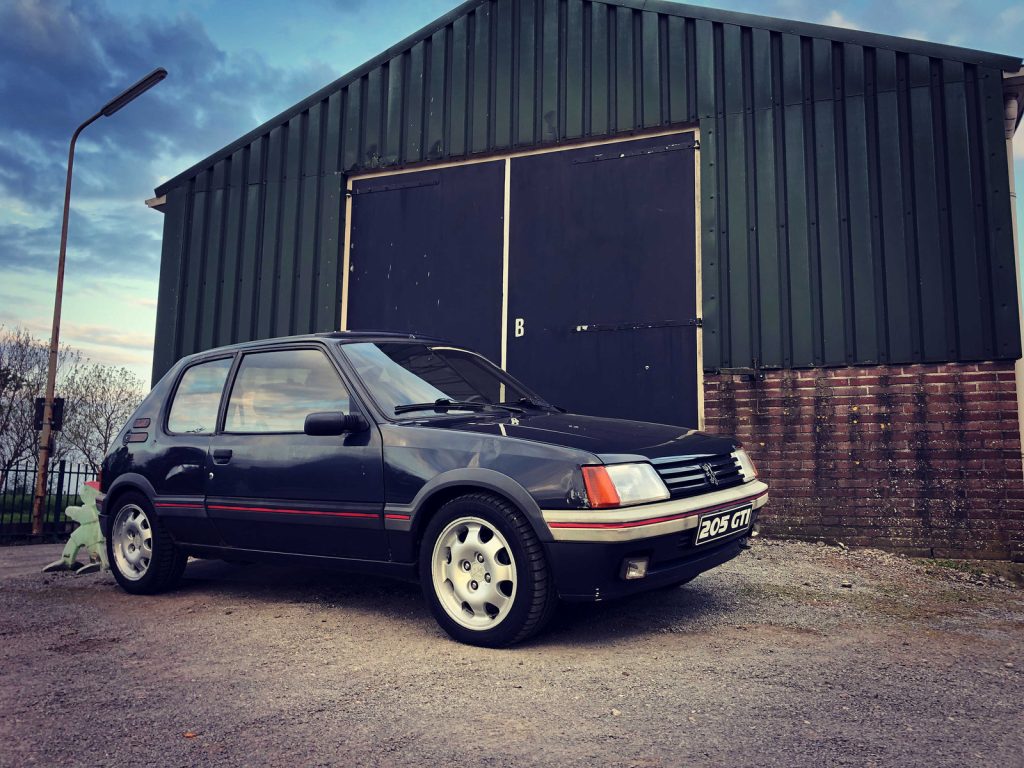 Peugeot 205 GTI 1.9 (130pk), driekwart van voren tegen een donkere gevel