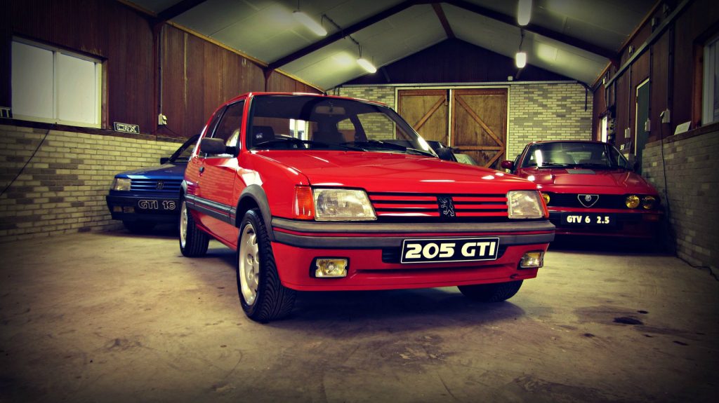 Peugeot 205 GTI 1.9 (130pk), driekwart van voren tegen een donkere gevel