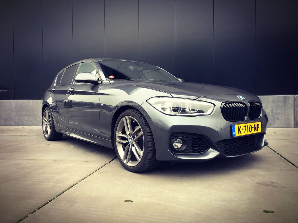 BMW 118i M-Sport (F20 LCI), driekwart van voren tegen een donkere gevel