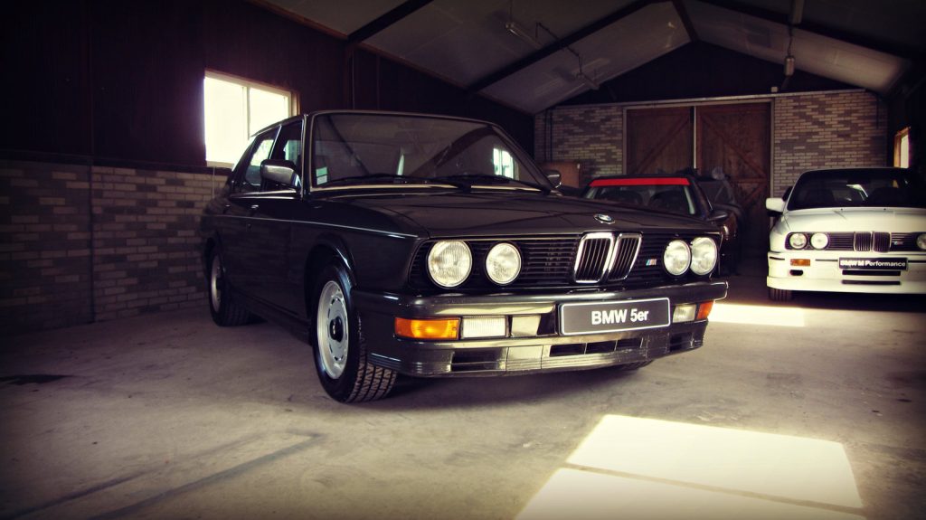 BMW M535i (E28), driekwart van voren tegen een donkere gevel