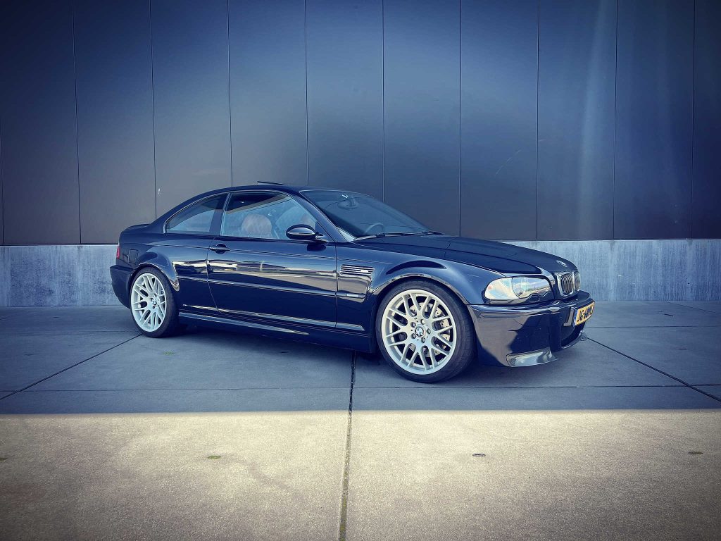 BMW M3 E46 in Carbonschwarz, driekwart van voren tegen een donkere gevel