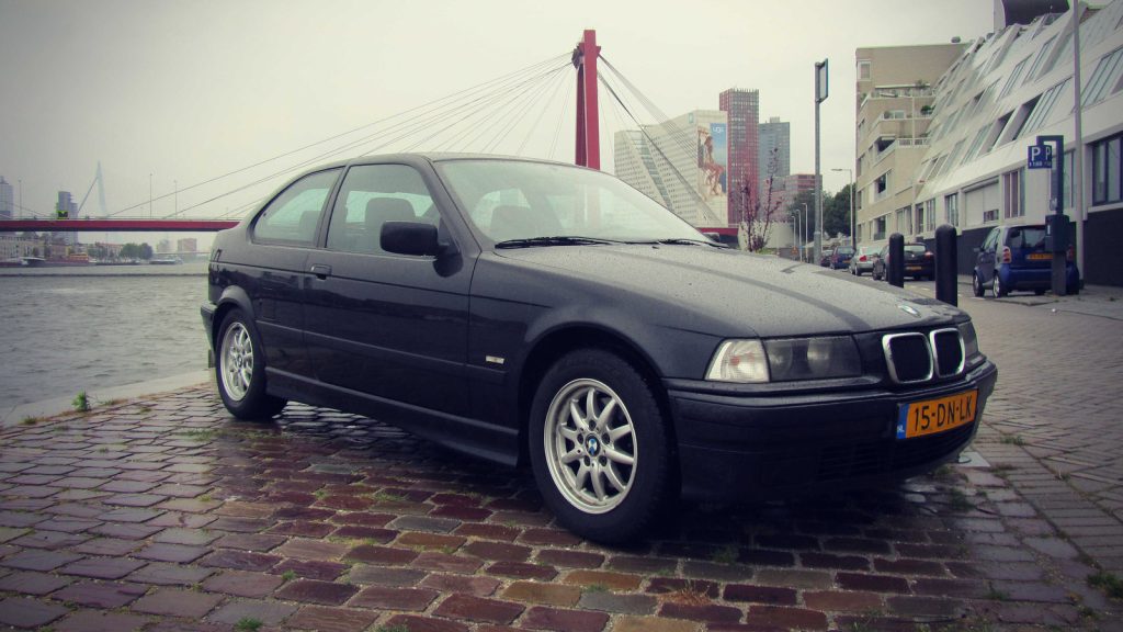 BMW 318tds Compact (E36 5), driekwart van voren tegen een donkere gevel