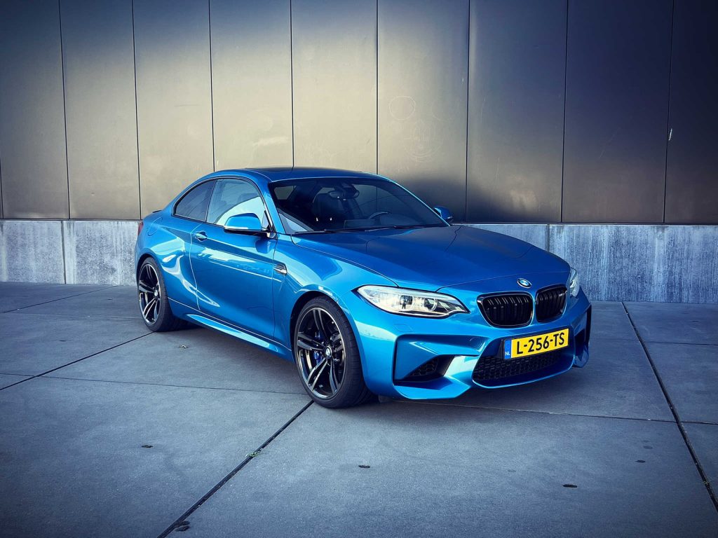 BMW M2 (F87), driekwart van voren tegen een donkere gevel
