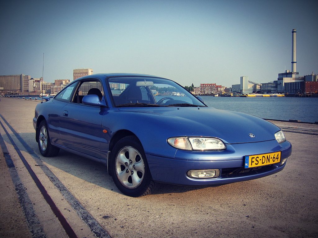 Mazda MX-6 2.5i V6, driekwart van voren tegen een donkere gevel