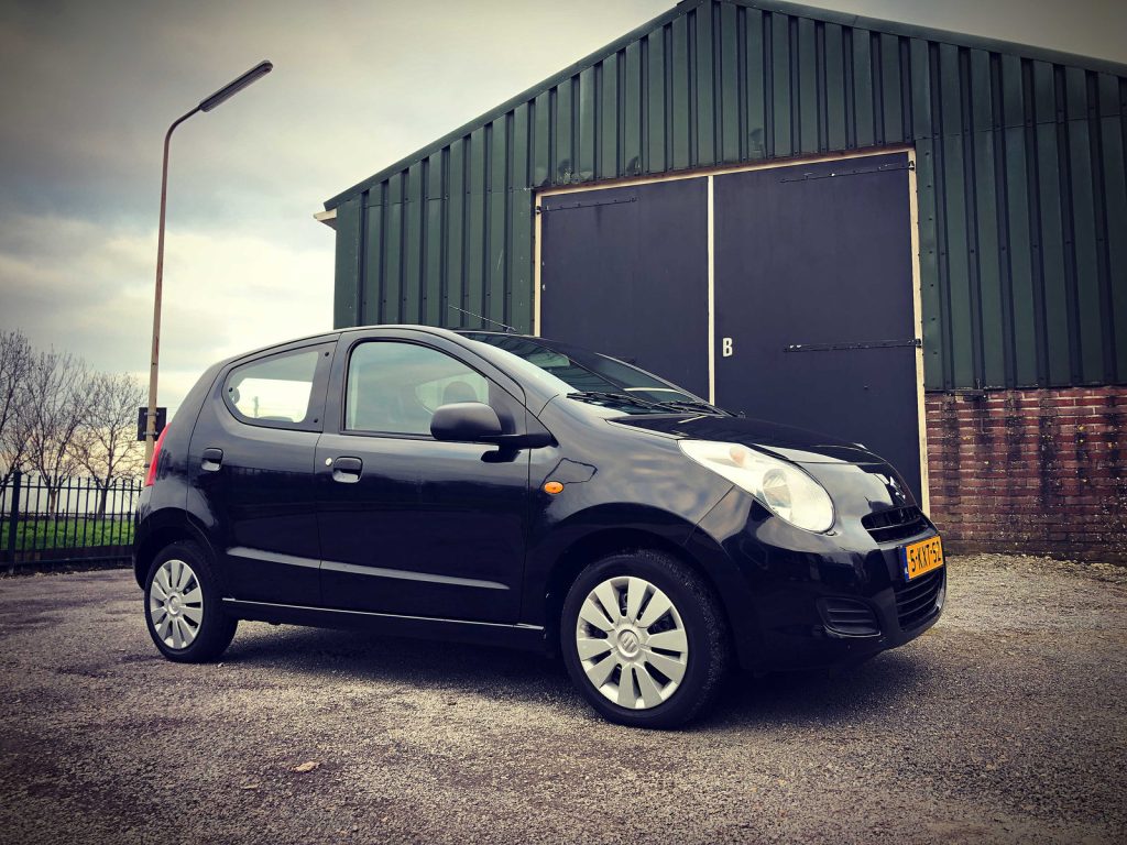 Suzuki Alto, driekwart van voren tegen een donkere gevel