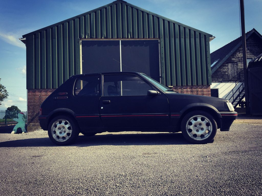 Peugeot 205 GTI 1.9, driekwart van voren tegen een donkere gevel