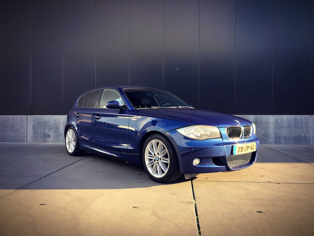 BMW 120i M-Sport (E87 LCI), driekwart van voren tegen een donkere gevel