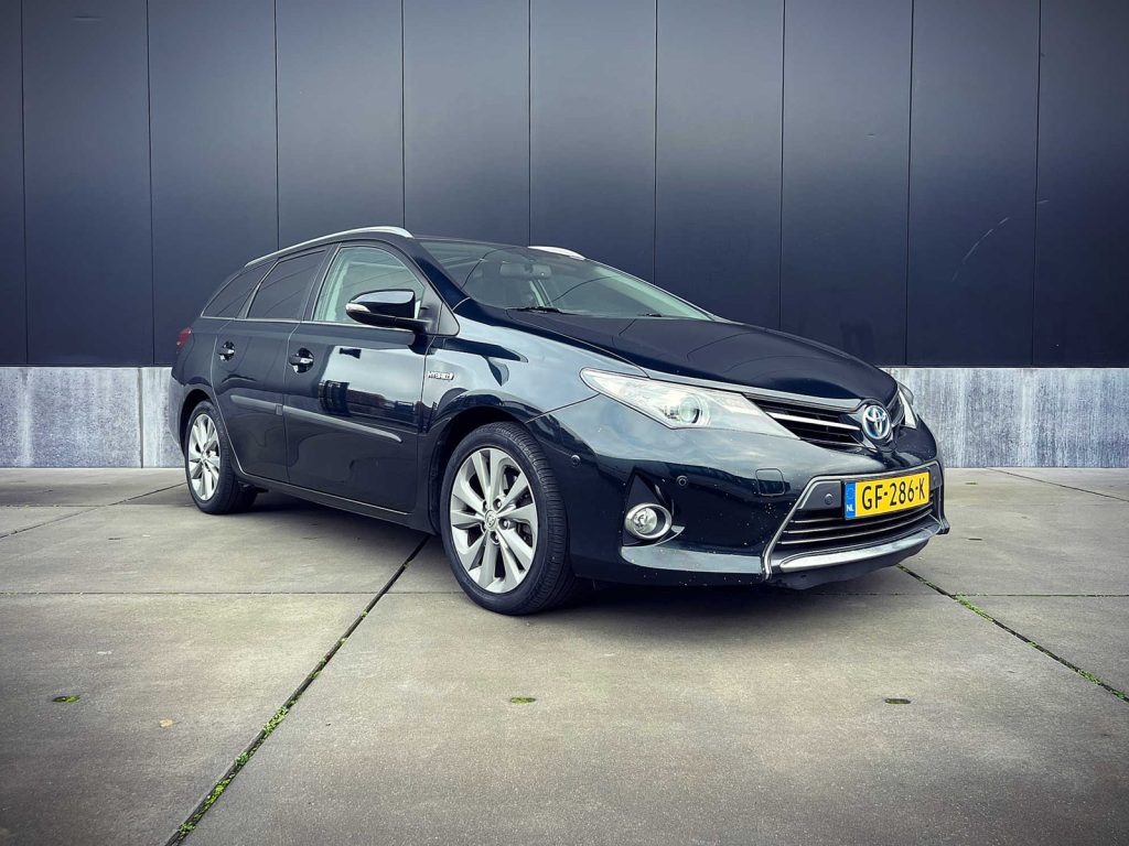 Toyota Auris Touring Sports 1.8 Hybrid, driekwart van voren tegen een donkere gevel