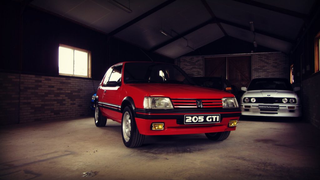 Peugeot 205 GTI 1.9, driekwart van voren tegen een donkere gevel