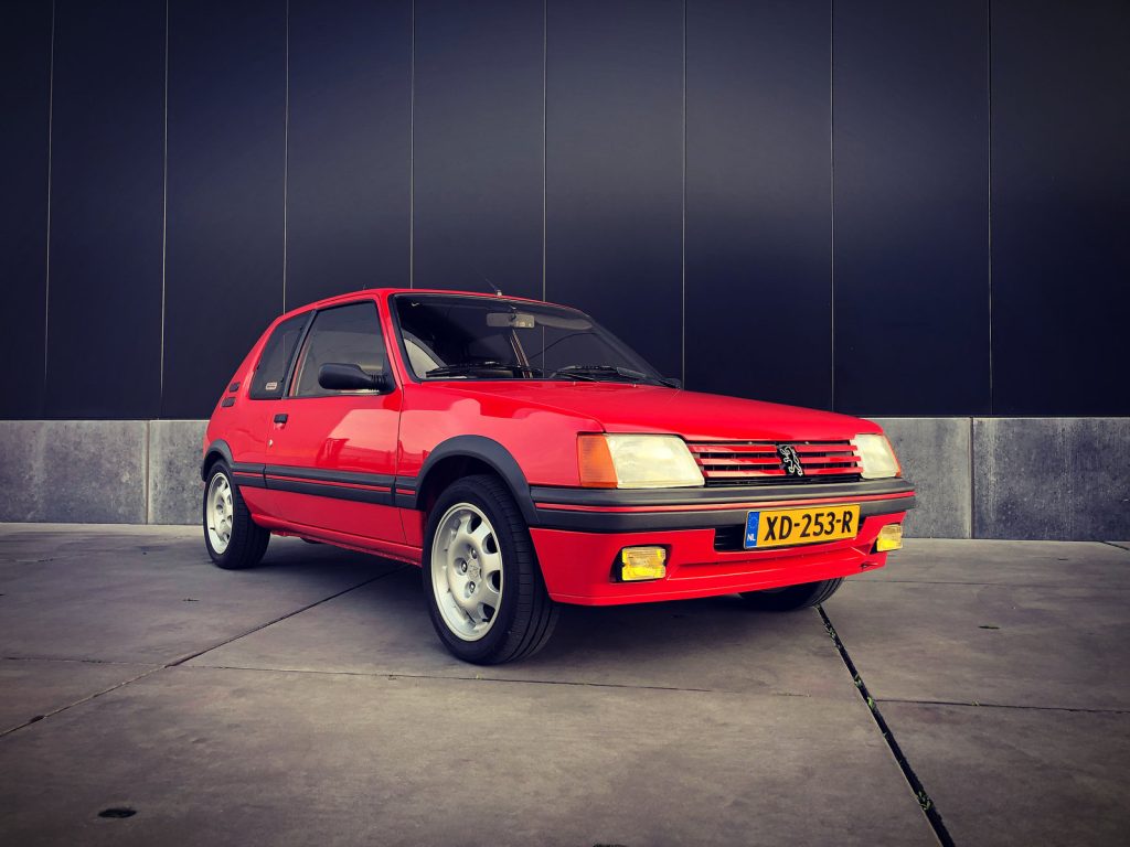 Peugeot 205 GTI 1.9 (130pk), driekwart van voren tegen een donkere gevel